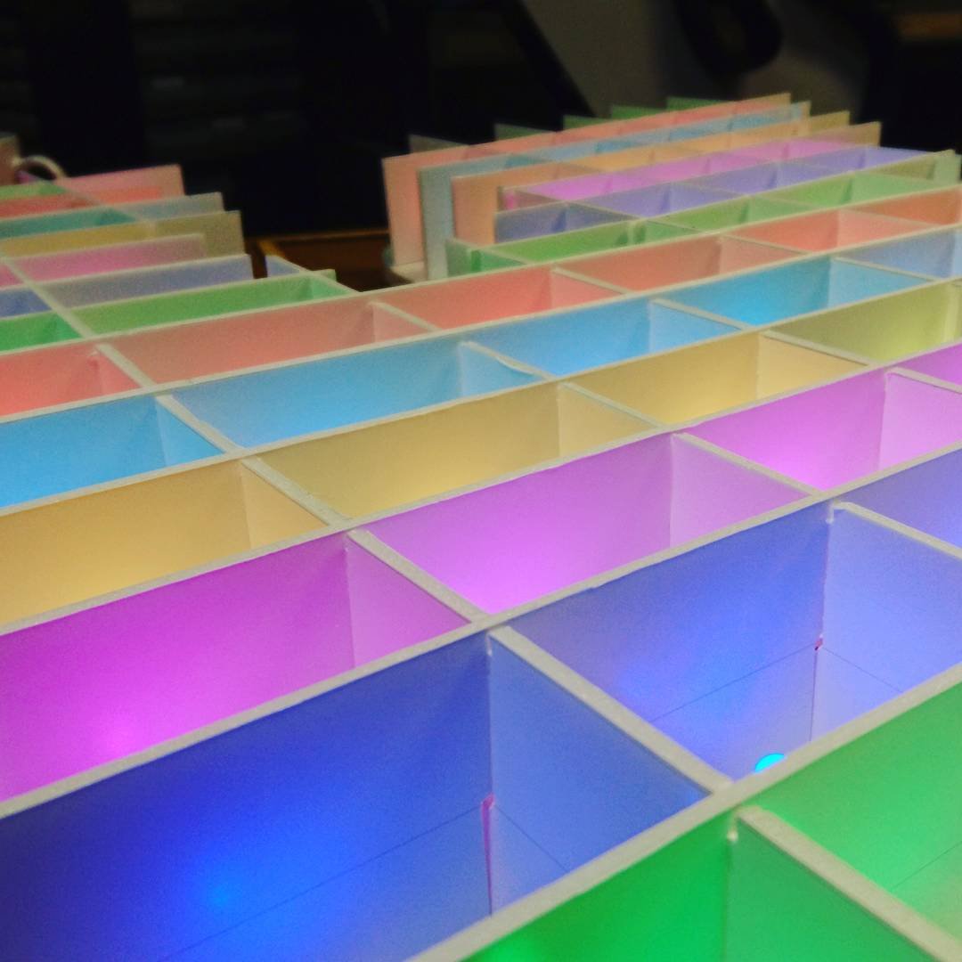 Oblique shot of a grid of rectangles made by intersecting foamcore walls.  The inside of each box in the grid is illuminated with coloured light, with the colours forming stripes across the image